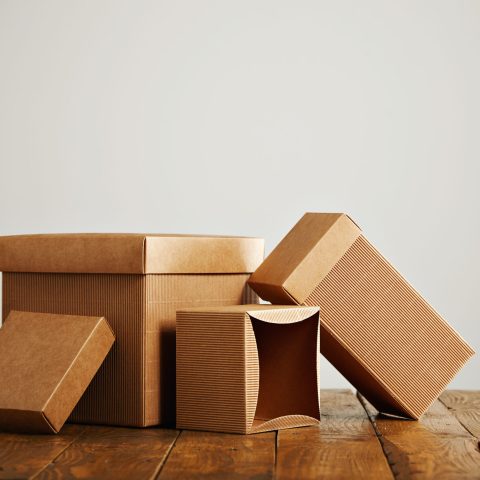 Set of three unlabeled similar craft cardboard boxes with covers beautifully arranged in a studio with white walls